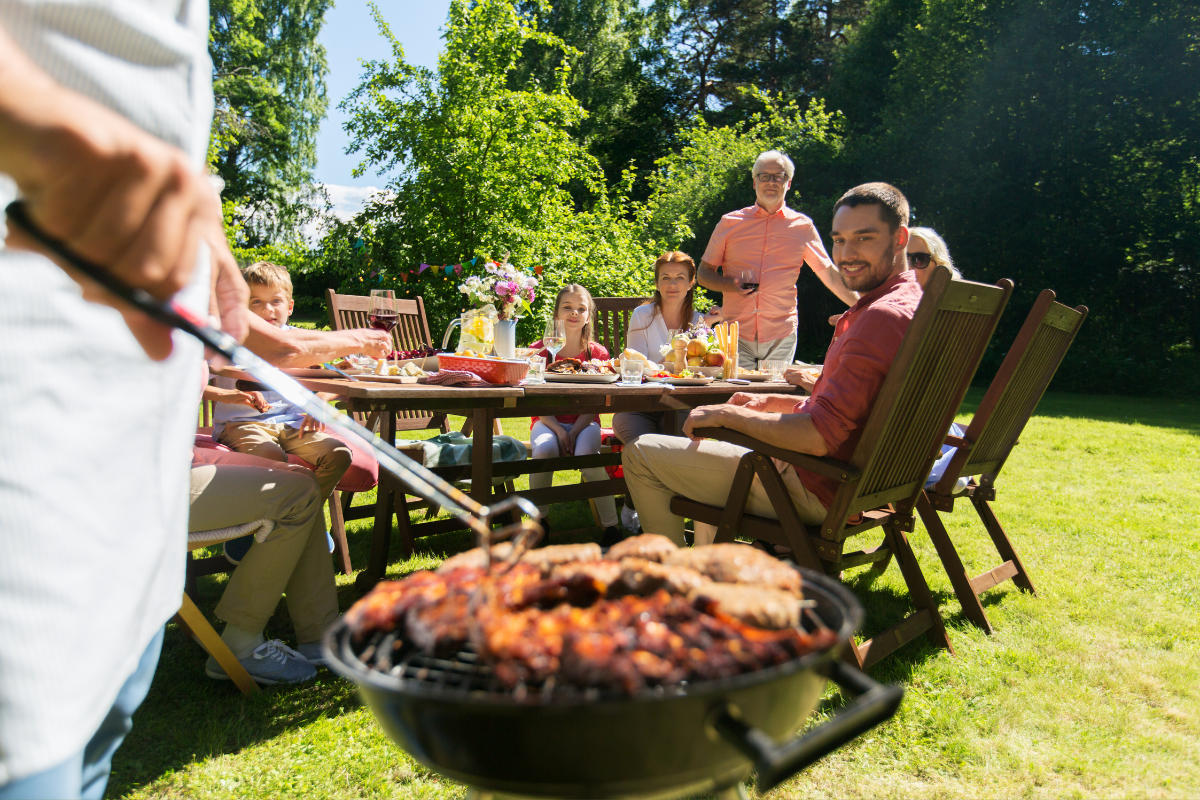 family sitting around a table outside while someone cooks food on the grill