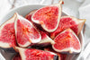 close-up of sliced vibrant figs in a white bowl on top of white table cloth
