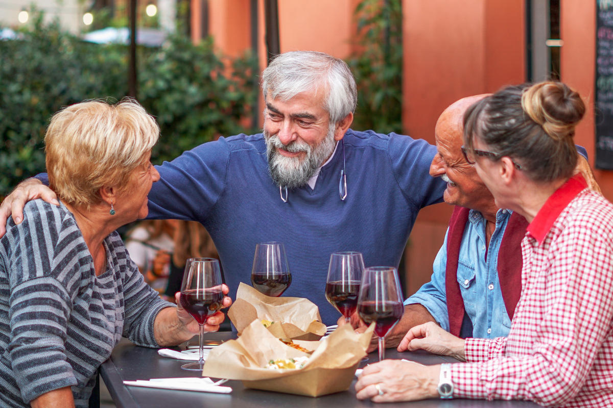 group of older friends gathered around a table, eating and talking, having a good time