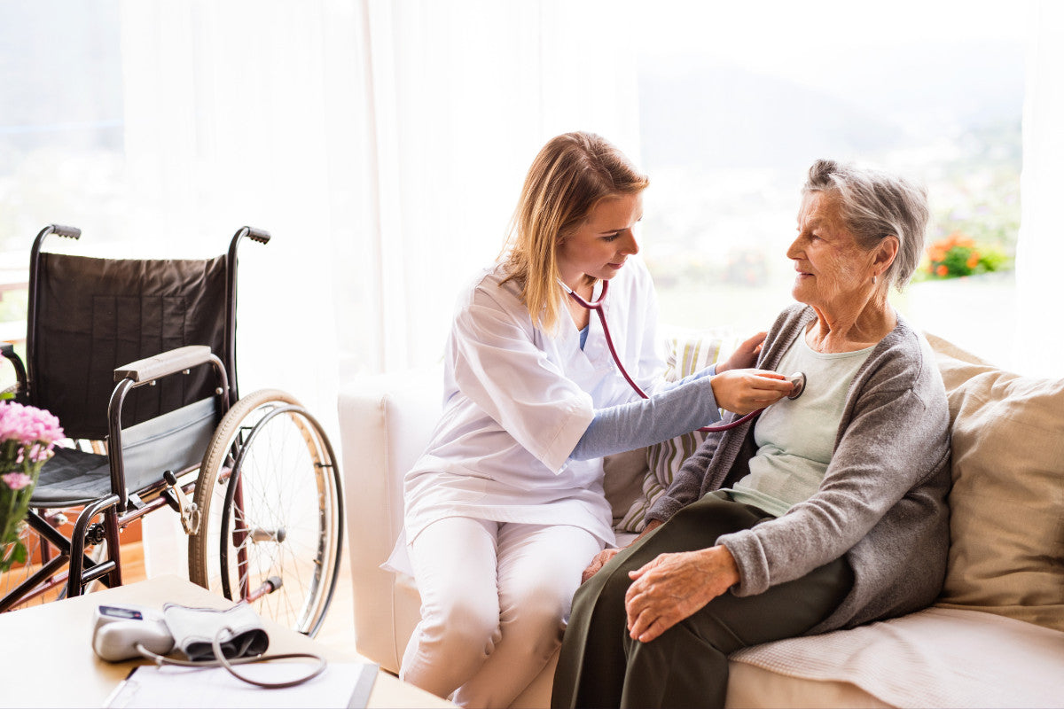 young nurse listening to a senior woman's heart while sitting on the couch