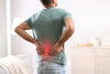 man standing in his room, holding his back because he's in pain