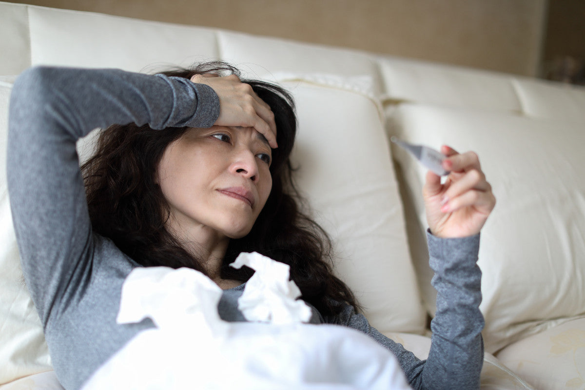 woman laying in bed with one hand on her head and the other holding a thermometer