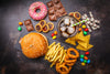 top view of various junk foods, including a cheeseburger, fries, onion rings, a donut, chocolate, candy, chips, etc.