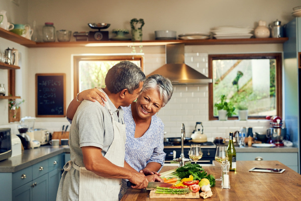 Senior couple smiling and enjoying cooking together in their kitchen.
