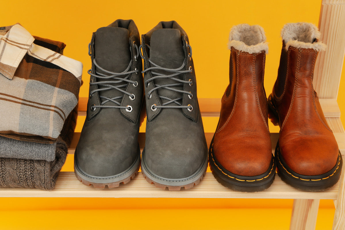 two pairs of boots sitting on a wooden bench against a yellow background.