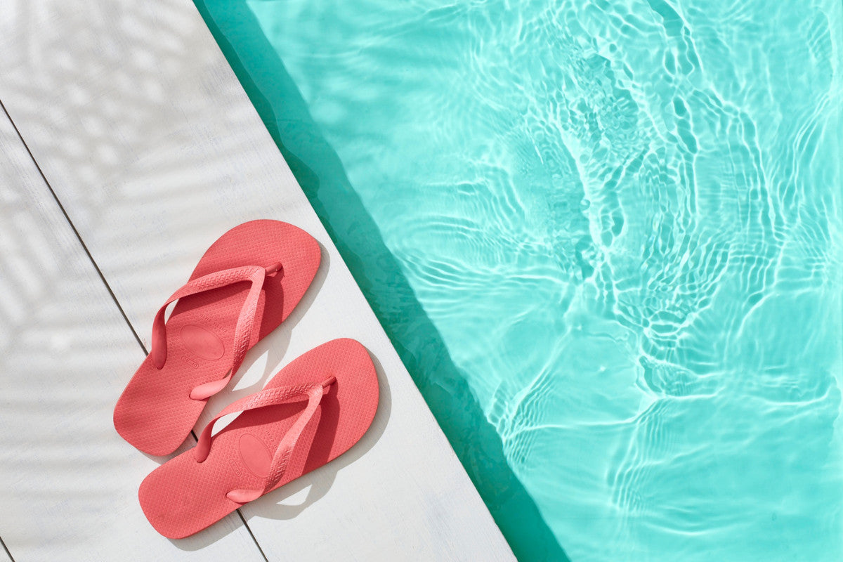 Pair of salmon-colored flip-flops sitting near the edge of a pool.