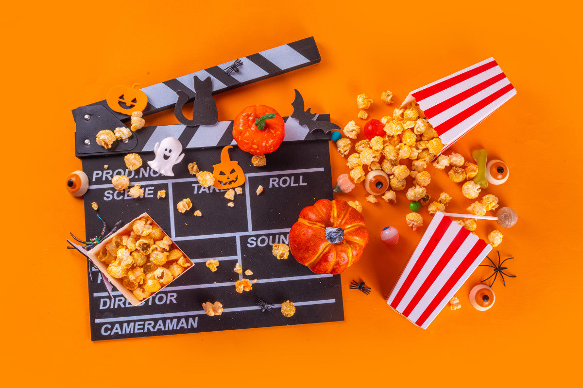 various Halloween snacks and popcorn with a movie clapperboard against a bright orange background.