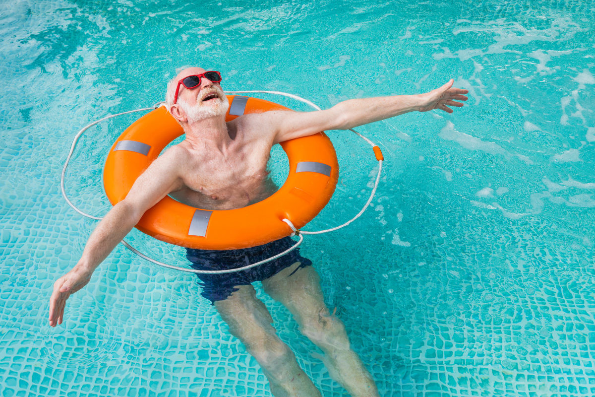 Senior man floating in an orange raft in a pool.