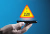 person's hand holding up a touchscreen phone with a warning triangle floating above it saying 