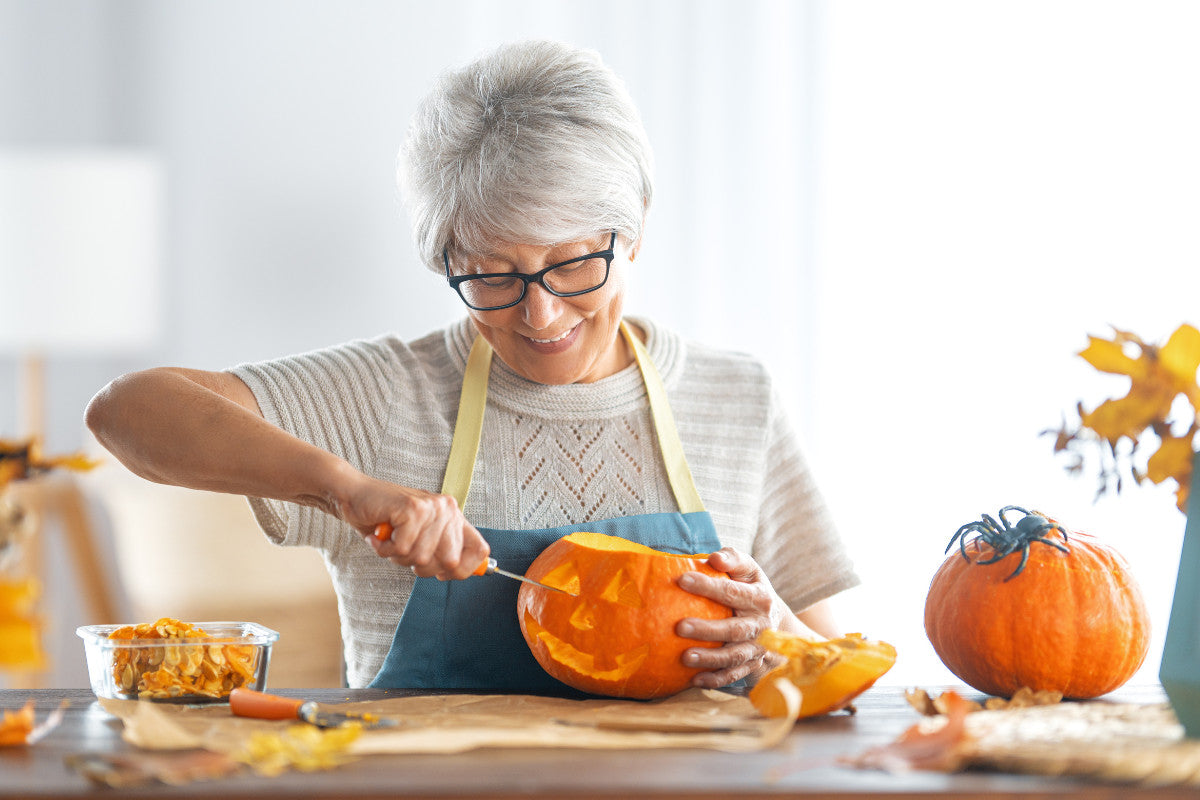 senior woman smiling as she carves a pumpkin.