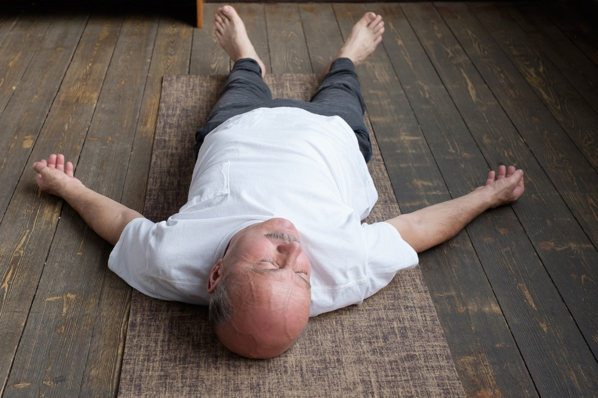 senior man laying on the floor on a yoga mat.