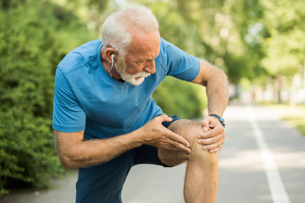 senior male runner, stopped to massage his knee while running outside.