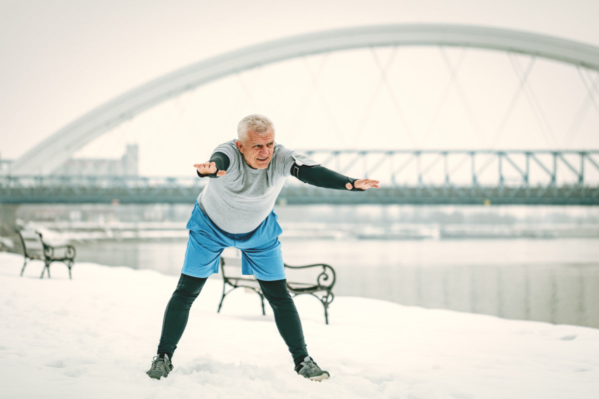 senior man stretching outside during winter. snow is on the ground.