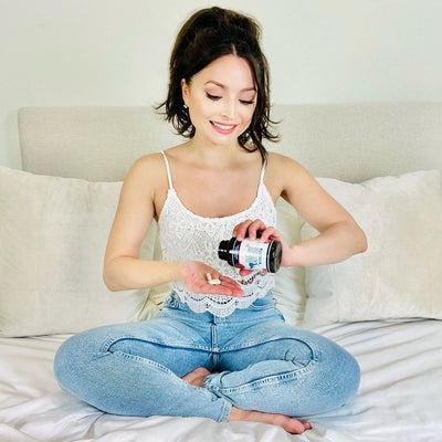 Woman sitting on a bed pouring Outback Magnesium+ capsules from the bottle into her hand