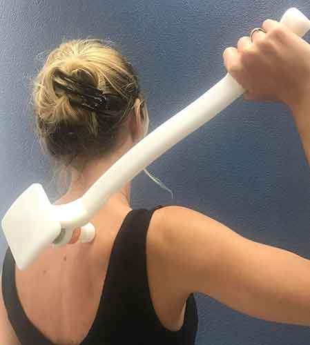 Woman reaching over her shoulder with the white Easy Reach Extender to apply to her upper back
