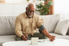 older man sitting on his couch at home, checking his blood pressure