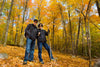 older couple hiking, smiling at camera in forest during fall. bright yellow leaves on trees