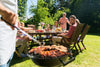 family sitting around a table outside while someone cooks food on the grill