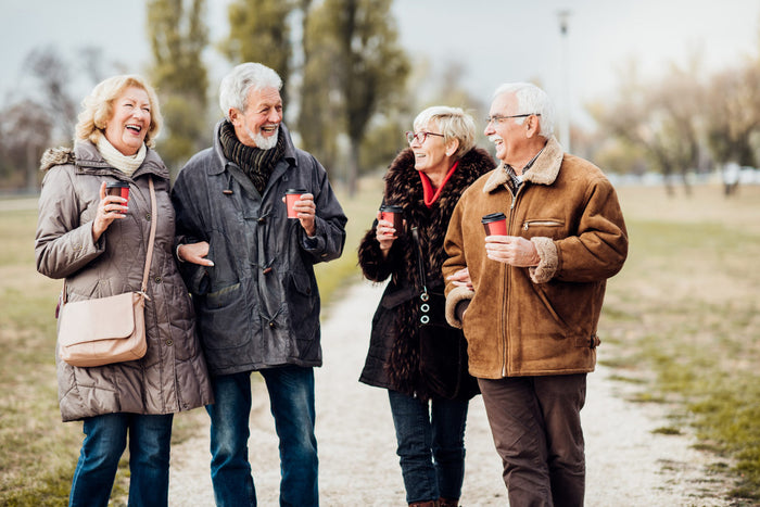 two couples smiling and laughing together, wearing coats outside drinking coffeee