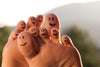 feet with sharpie smiley faces on the back of the toes on blurry outside background