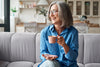 older woman smiling, sitting on couch with cup of coffee