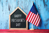 Happy Presidents day written on black chalkboard with a small American flag standing next to it