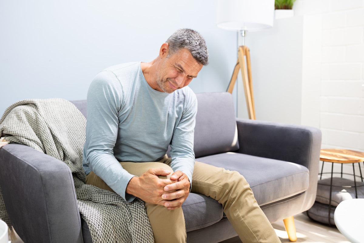older man sitting on the couch holding his knee in pain