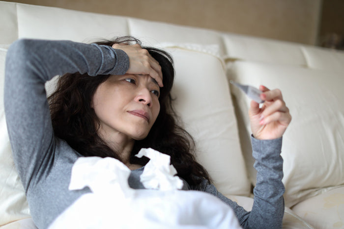 woman laying in bed with one hand on her head and the other holding a thermometer