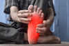 Close-up of older man holding his foot, showing redness to represent neuropathy.
