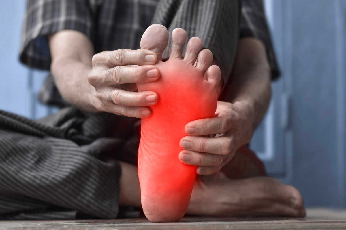 Close-up of older man holding his foot, showing redness to represent neuropathy.