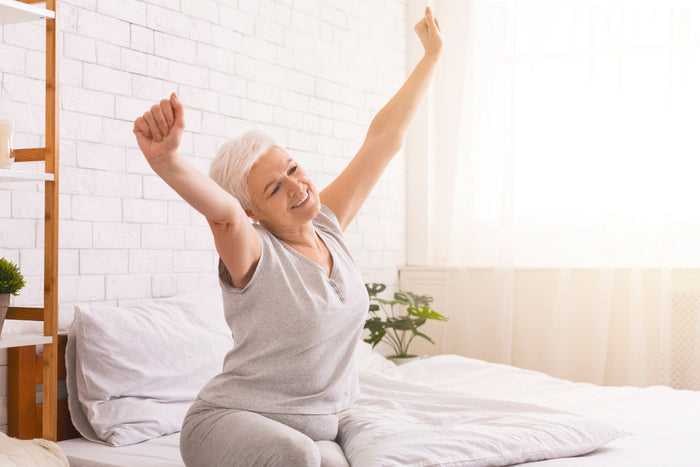 Senior woman stretching in bed after waking up in the morning.