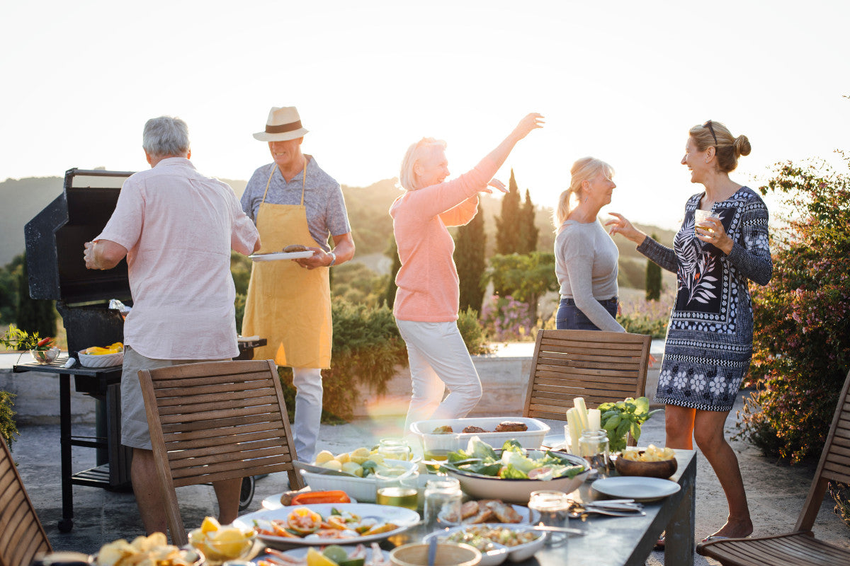 Group of seniors dancing around a grill and table on a beach.