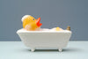 a yellow rubber ducky relaxing in a small bubble bath. light blue flooring and dark gray-blue wall.