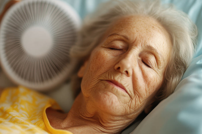Senior woman holding a small white fan while she sleeps.
