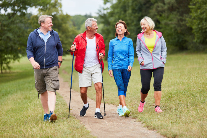Group of 4 seniors walking and laughing together outside on a dirt trail.