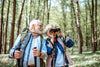 older couple hiking in the woods stopped to look through binoculars