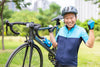 older male cyclist smiling as he shows his strength by holding up his bicycle on the grass outside