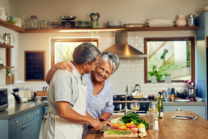 Senior couple smiling and enjoying cooking together in their kitchen.