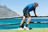 senior man leaning against a wooden rail lined against a lake as he gets a sudden cramp in his calf.