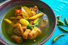 bowl of turmeric chicken soup on a light blue background.