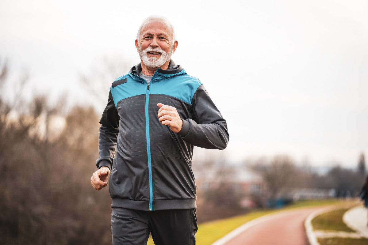 senior man wearing long sleeve workout clothes, running on track outside in the fall.