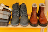 two pairs of boots sitting on a wooden bench against a yellow background.