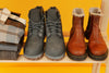 two pairs of boots sitting on a wooden bench against a yellow background.