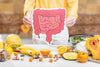 someone holding up a cutout of a healthy gut, above a counter covered with various gut-healthy foods.