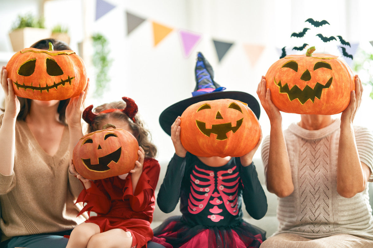 family of four holding jack-o-lanterns in front of their faces. the kids are wearing costumes.
