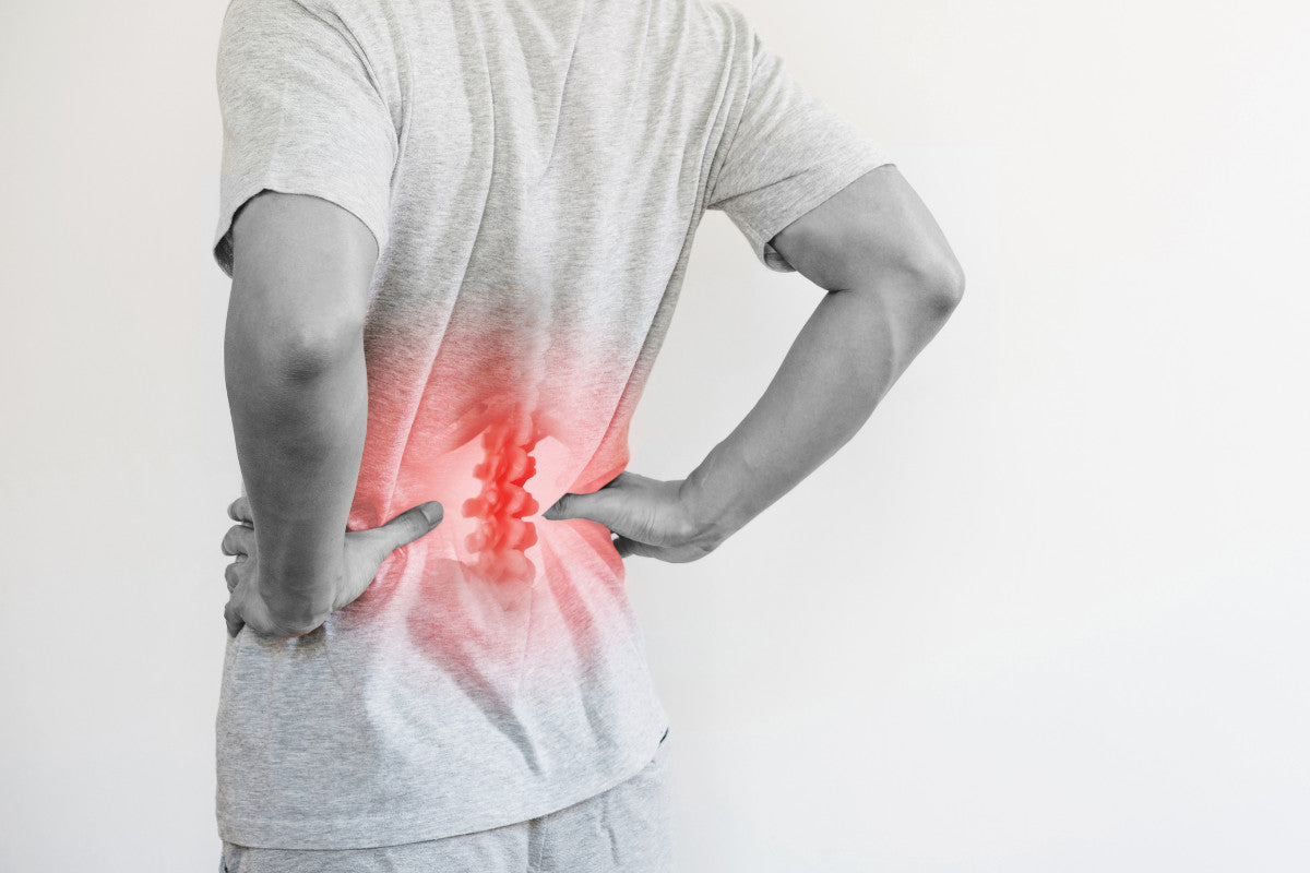 black and white image. back view of a man with his hands on his hips and lower back. red, inflamed spine can be seen through his shirt. 