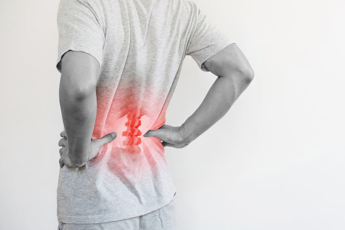 black and white image. back view of a man with his hands on his hips and lower back. red, inflamed spine can be seen through his shirt. 