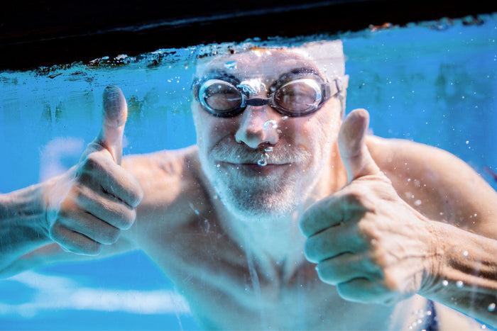 Senior man swimming underwater giving a thumbs up.