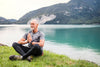senior man meditating by a lake.