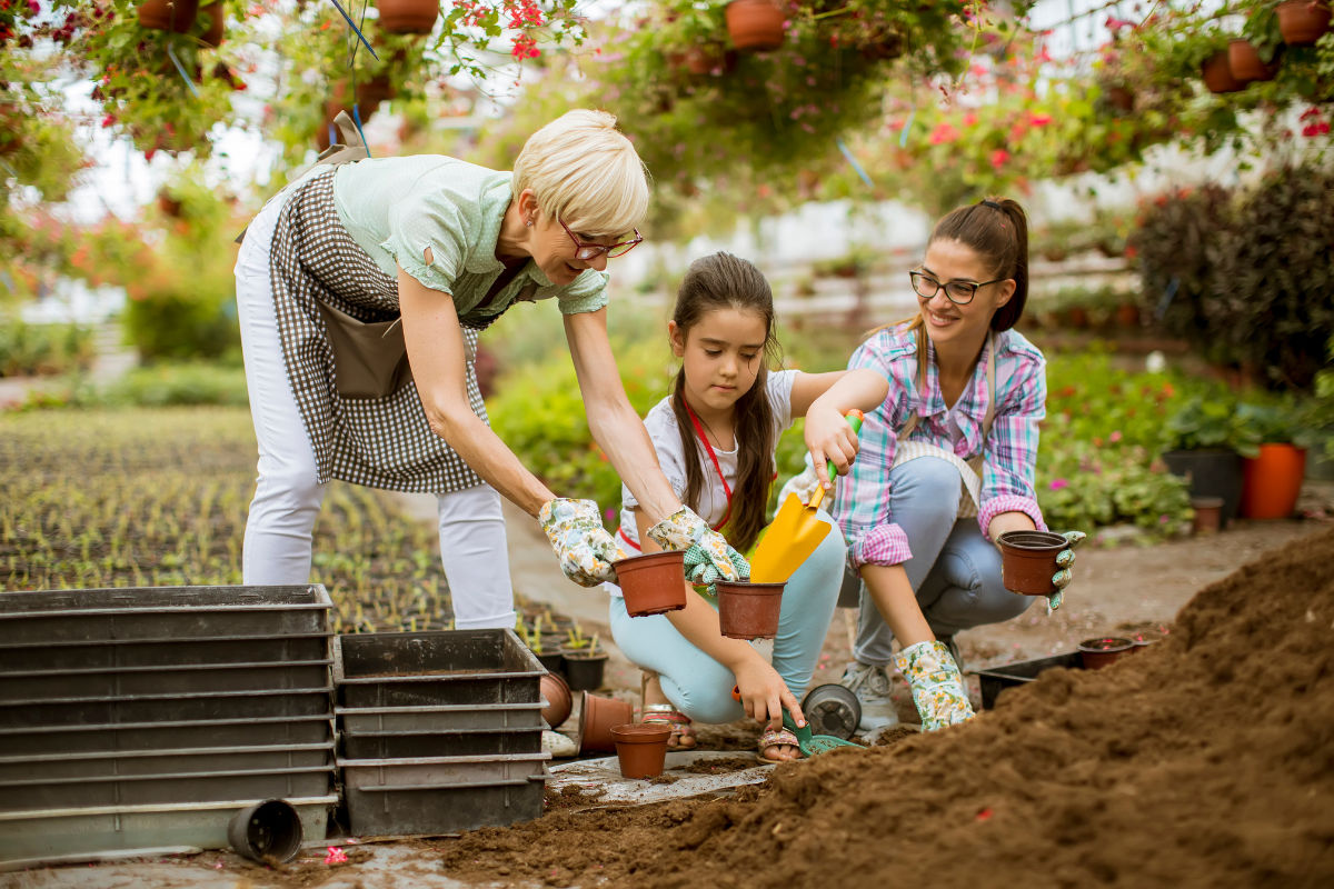 older woman helping her grandkids plant flowers in pots outside.